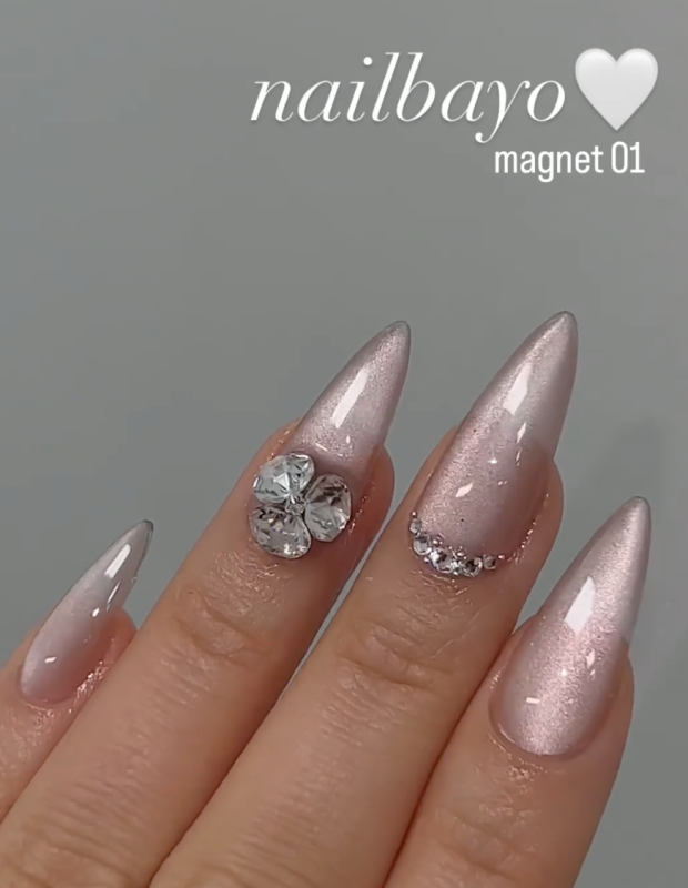 Detailed alt text for the image of the Nailbayo DOI Magnet Gel #1 - 10ml product:
Elegant and intricate nail art adorned with the Nailbayo Magnet Gel #01, a premium Korean nail product featuring a stunning floral design accented by sparkling rhinestones. The nails showcase a lustrous, metallic pink finish that shimmers under the light, creating a captivating and visually striking appearance. This specialized gel formula requires the use of a mag