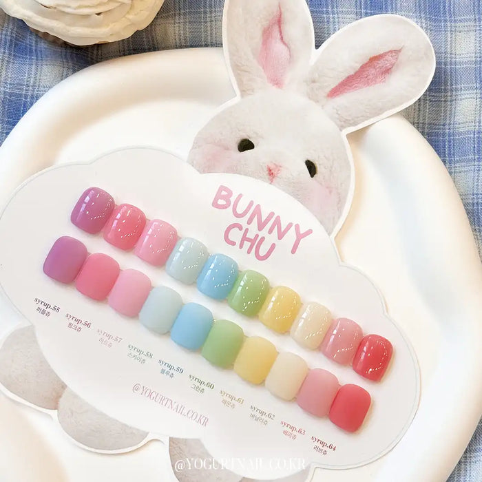 Soft, pastel-colored nail polish gels in various shades, displayed on a plate with a cute bunny-shaped container. The image showcases the "Bunny Chu Collection" of nail care products by the Shopify brand, highlighting the sheer, smooth gradient effects and the diverse range of spring-inspired colors available.