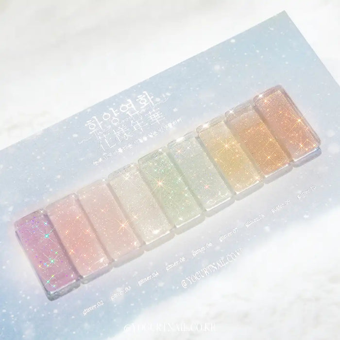 Delicate pastel-colored glitter gel bottles displayed on a snowy, sparkling background with limited edition packaging, showcasing the "Yogurt In The Mood For Love Collection" by the Shopify brand. The image highlights the dazzling, subtle shine and variety of shimmering colors in the full set, perfect for enhancing toned gel nail polish.