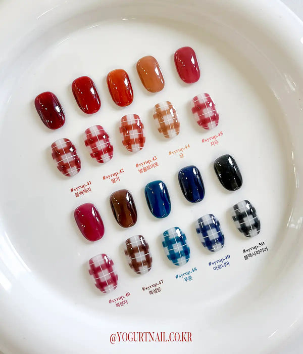 Image alt text: A collection of colorful gel nail polish shades in various hues, including deep reds, oranges, browns, and blues, displayed on a white tray. The nail polish bottles are labeled with their corresponding color names and product codes, showcasing the Yogurt Tanghulu Collection.