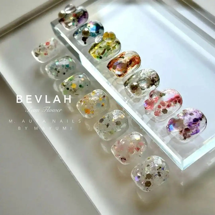 Dazzling and vibrant floral gel nail products from the BEVLAH I Am Flower collection, featuring an array of natural dried flowers and glitter inclusions that create a unique and visually captivating design for each individual nail. The varied sizes, shapes, and types of flowers within the set add an element of organic beauty and customization to this luxurious nail care offering.