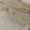 A promotional image featuring the 'Smoothie Fresh Pastel Tone Collection' by MUSE, displaying a variety of nail polish swatches in soft pastel colors, labeled with names such as 'White sand,' 'Forsythia,' and 'Surf crest,' presented elegantly on a promotional booklet decorated with citrus fruit illustrations.