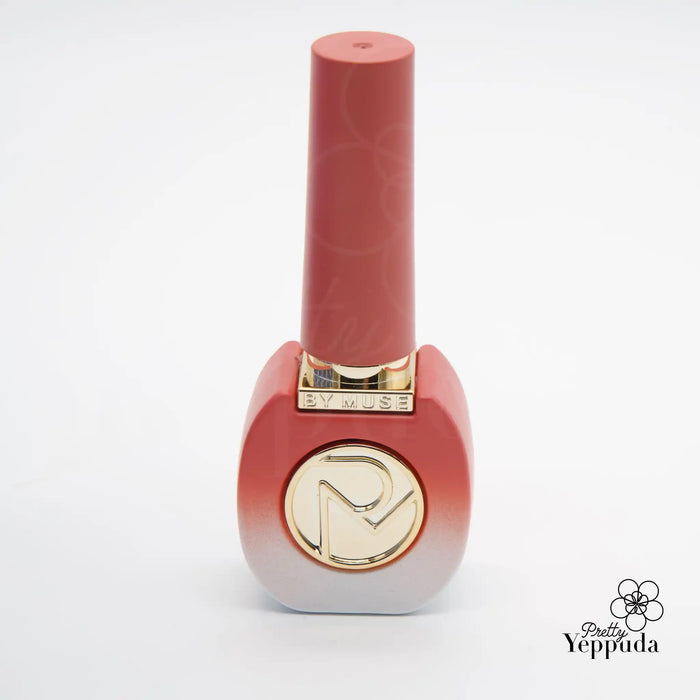 A vibrant, coral-colored nail polish bottle with the brand name "BY MUSE" prominently displayed on the cap, featuring a stylized gold-tone logo design.