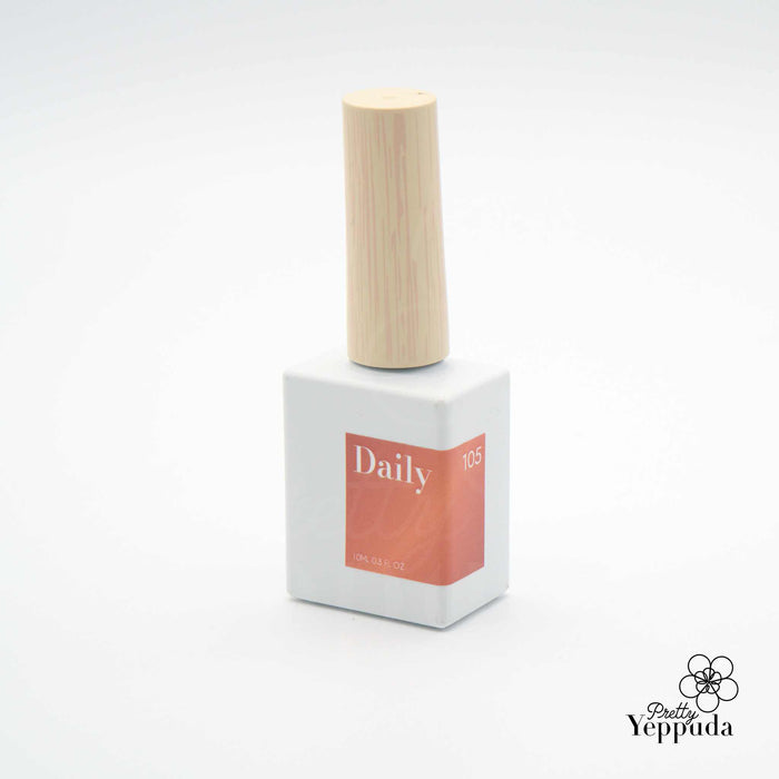 A wooden bottle of nail polish from the DAILY 'WOODY' Collection, showcasing the warm and autumnal color palette of the 10-piece set. The bottle features a simple, minimalist design with a neutral-toned wooden cap, drawing attention to the vibrant nail polish colors within.