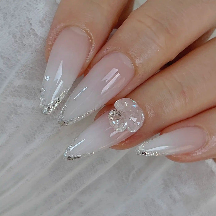 Elegant long nails featuring an ombre design using NAILBAYO DOI Aube #1, enhanced with delicate silver glitter at the tips and a large 3D crystal embellishment on the ring finger. The design combines simplicity with a luxurious sparkle.