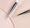 Close-up of JELLO JELLO Dual Line Brush set featuring two precision brushes with sleek silver and black handles. One brush has a thicker tip while the other has a finer point, both resting on a soft pink background, showcasing their versatility for detailed nail art and design work.