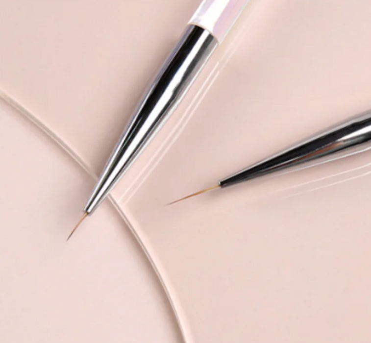 Close-up of JELLO JELLO Dual Line Brush set featuring two precision brushes with sleek silver and black handles. One brush has a thicker tip while the other has a finer point, both resting on a soft pink background, showcasing their versatility for detailed nail art and design work.