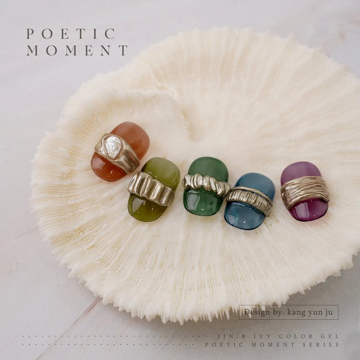 10 vibrant and translucent nail polish bottles in a variety of fall-inspired hues, including orange, green, and purple, resting on a soft, fluffy white surface, evoking a serene and poetic aesthetic for the JIN.B Poetic Moment Collection.