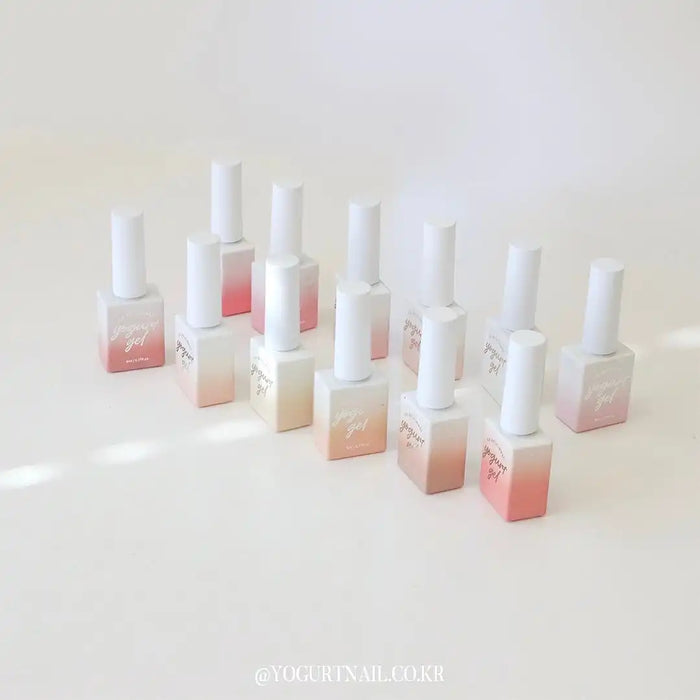 Twelve pearlescent bottles containing soft pink and white nail gel polishes from the Yogurt Blossom Ending Collection, showcasing the natural, self-leveling formula and mid-viscosity texture. The minimalist and elegant packaging design highlights the Yogurt Nail Kir brand.