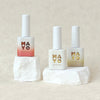 Three bottles of MAYO Eros Collection gel nail polish, featuring a range of shades inspired by the goddess of love, including delicate pinks, fiery oranges, serene greens, and golden hues. The bottles are displayed on white marble-like pedestals, showcasing the premium quality and elegant design of the MAYO brand.