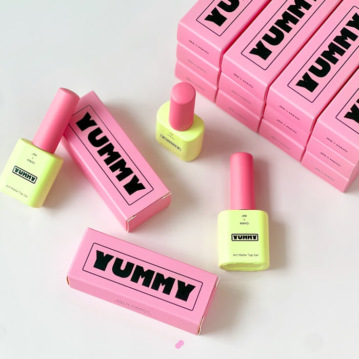 A promotional image showcasing Yummy Art Matte Top Gel bottles arranged in a visually appealing pattern against a background of pink boxes labeled 'YUMMY.' The vibrant colors of the packaging highlight the product's branding.