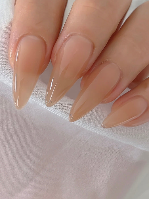 A close-up image of manicured, glossy nude-colored nails with a natural, healthy sheen. The nails are shaped into a pointed, elongated style, creating a sleek and sophisticated look. The image showcases the superior quality and seamless application of the NAILBAYO DOI Nudi Gel Hazelnut product, highlighting its ability to deliver a flawless, long-lasting nail color and finish.