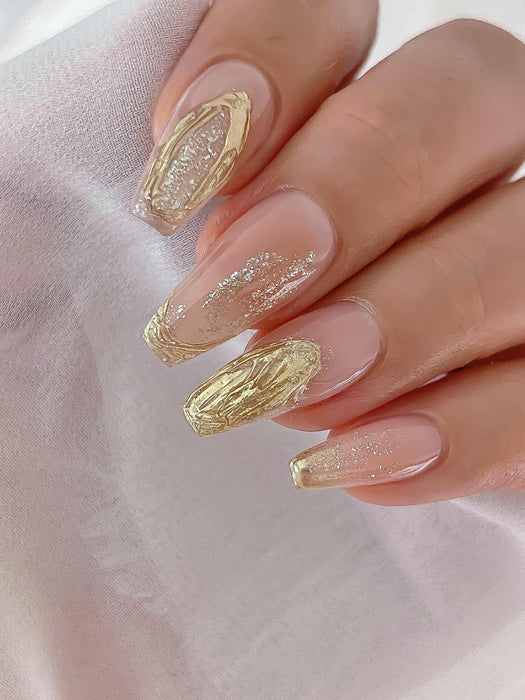 Elegant manicure featuring long coffin nails with a combination of nude base, gold foil accents, and glitter details. The nails showcase intricate designs, including swirled gold patterns and sparkling elements, demonstrating the versatility and beauty of Nailbayo DOI Thick Gel for creating luxurious and sophisticated nail art.