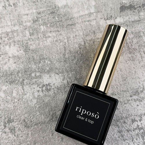 A clear and top gel product with the brand name "RIPOSO" displayed prominently on the bottle, which is resting on a textured gray background. The bottle has a sleek, cylindrical design with a metallic top, conveying a premium and high-quality aesthetic.