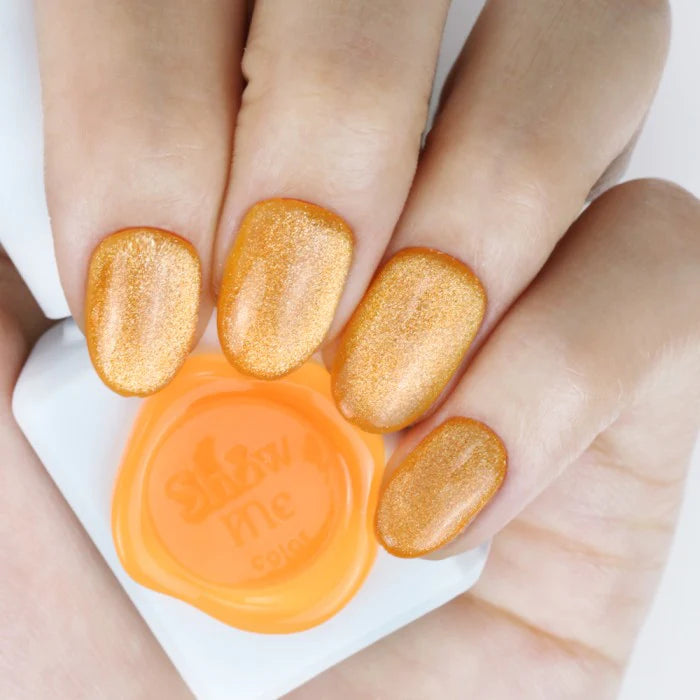 A close-up image showcasing a set of vibrant, cateye-shaped nails painted in a bold, golden-orange hue. The nails are complemented by an orange nail polish bottle, highlighting the "Show Me Korea" brand and the "Cooing Punch Cat Eye Gel Series" product.