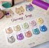 Colorful, stylized cat faces in a variety of soft, vintage-inspired shades, showcasing the "Purring Song" nail gel collection by the renowned Korean brand SHOWME Korea. This product set features 10 solid color gel polishes that offer a one-swipe, high-pigment application, curing under UV/LED light for a long-lasting, professional finish.