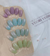 Elegant display of assorted gel nail polish shades from the Yeori Yeori Collection by Show Me Korea, showcasing a variety of translucent and pearlescent hues in pastel tones of purple, blue, and green, arranged on a wooden palette.