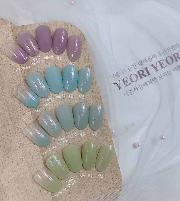 Elegant display of assorted gel nail polish shades from the Yeori Yeori Collection by Show Me Korea, showcasing a variety of translucent and pearlescent hues in pastel tones of purple, blue, and green, arranged on a wooden palette.