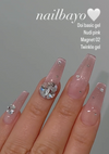 Detailed alt text for the Nailbayo Doi Magnet Gel #2 - 10ml product image: The image shows a close-up of human hands with neatly manicured, light pink gel nails. The nails have a glossy, sparkly finish, and some are adorned with small, shimmering crystal accents. The product name "Nailbayo" is prominently displayed in white text at the top of the image, along with a heart icon. The gel product is described as a "Doi basic gel" in a "Nudi pink" sh