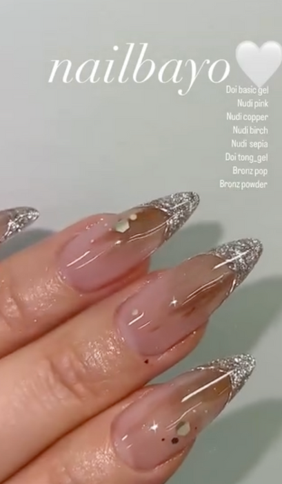 A high-quality, close-up image of a hand featuring beautifully manicured, artificial nails in a shimmering copper color. The nails are long, with intricate nail art designs. The image showcases the exceptional craftsmanship and attention to detail of the Nailbayo DOI Nudi Gel Copper - 10ml product, highlighting its versatility and suitability for both professional and beginner nail enthusiasts.