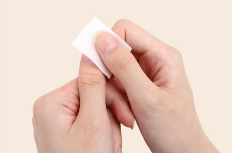 A close-up image of a person's hands gently applying or removing a white nail pad or wipe, showcasing the convenience and ease of use of the Jello Jello To Go Nail Pad product, which is designed to provide a quick and effective gel cleanser solution for nail care on the go, as described in the product description.