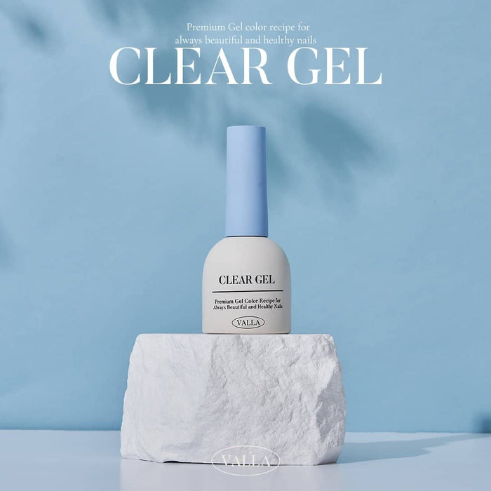 Promotional image of VALLA Clear Gel nail polish displayed on a rocky base against a soft blue background. The label reads 'Premium Gel Color Recipe for always beautiful and healthy nails', emphasizing its premium quality and benefits.