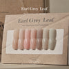 Display of VALLA Earl Grey Leaf collection swatches on a rustic paper background, showcasing a range of nine nail colors from soft pink to earthy gray, each labeled with its unique shade number.