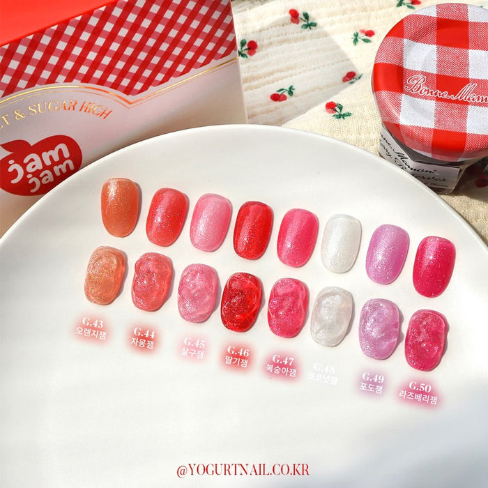 Eight vibrant and shimmering jelly-like nail polish products in a variety of red, pink, and white hues, resembling the luscious and juicy textures of fruit jams and syrups, displayed on a white plate with a gingham-patterned cloth in the background, creating a visually appealing and appetizing presentation for the "YOGURT JAM JAM Collection" Shopify product.