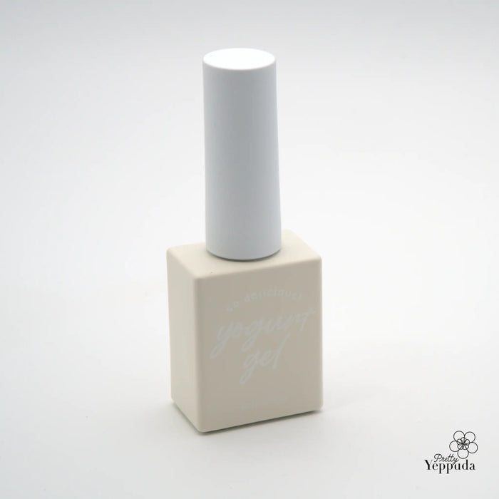 A minimalist, white cylindrical nail polish bottle sits atop a beige square-shaped base, highlighting the simple yet elegant design of this YOGURT Grocery set product. The clean, modern aesthetic showcases the high-quality, neutral-colored packaging that would complement a variety of home decor and personal styling preferences.