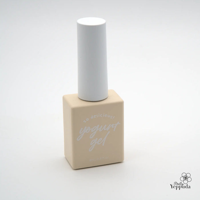 Detailed image of a minimalist, beige-colored nail polish bottle with a white cap, showcasing the simple and elegant design of this Shopify product from the "Yogurt" brand.