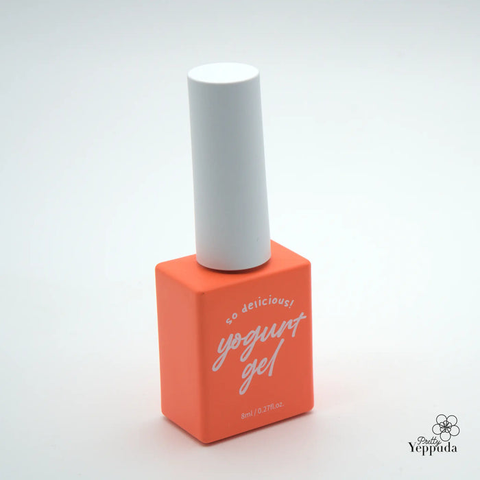 A vibrant orange nail polish bottle with a white cap, prominently displaying the brand name "Yogurt gel" in stylish text. The product appears to be part of a grocery-themed collection, offering a wide range of 90 color options for a personalized and indulgent nail care experience.