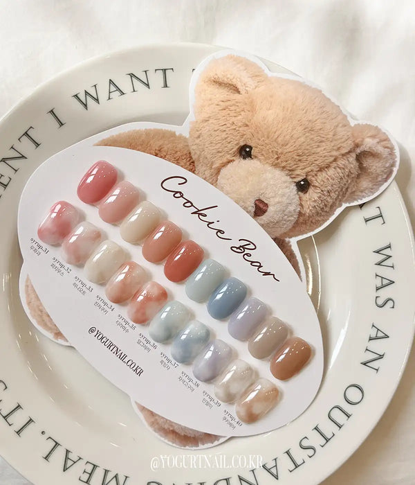 Soft, cuddly teddy bear beside a colorful display of nail polish shades from the Cookie Bear Collection, showcasing the warm, mulled shades and buildable formula of this Yogurt brand nail product line.