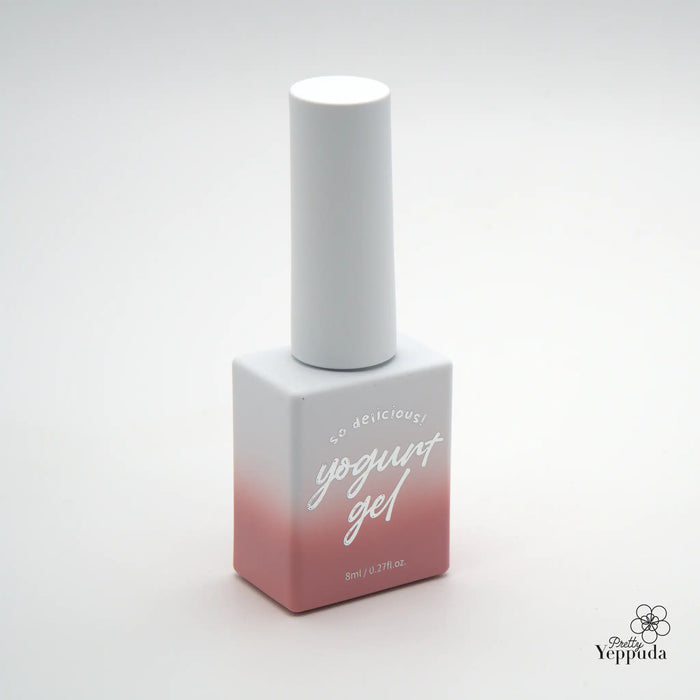 The alt text for this image of the Yogurt Blossom Ending Collection 12 syrup gels product could be: "A white and pink bottle of Yogurt Nail Gel polish featuring a high-quality, self-leveling formula that blends seamlessly with the natural tone of the nails. The gel polish belongs to the Blossom Ending Collection, which offers 12 lovely, natural shades.