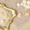 Charming 3D Hoholee and Riri nail charms and stickers adorn a golden nail decor in this whimsical product image, showcasing the playful and adorable designs of the Hoholee x Make.n Charm and Sticker Pack. This visually appealing product shot highlights the unique and delightful nail accessories that can elevate one's nail game with a touch of irresistible cuteness.