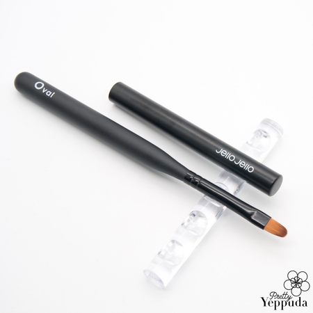 Detailed alt text for the "JELLO JELLO Flexible Brush Oval" Shopify product image: The image shows a black oval-shaped makeup brush with the JELLO JELLO brand name printed on it. The brush has a flexible bristle design, making it suitable for creating beautiful gel nail art and designs. The product's sleek, modern appearance and ergonomic shape suggest its versatility and ease of use for professional-quality nail care.