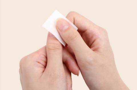A close-up image of a person's hands gently applying or removing a white nail pad or wipe, showcasing the convenience and ease of use of the Jello Jello To Go Nail Pad product, which is designed to provide a quick and effective gel cleanser solution for nail care on the go, as described in the product description.