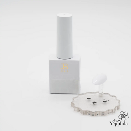 Elegant white bottle of JIN.B IVY Color Gel White nail polish, featuring minimalist design with gold lettering. Accompanied by a transparent flower-shaped palette and applicator brush, showcasing the product's professional quality and attention to detail for precise nail art application.
