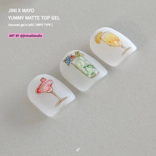 Close-up of three artificial nail tips decorated with intricate cocktail designs using JINI X MAYO Yummy Matte Top Gel. The nails feature a pink martini, a green mojito, and a yellow mimosa, showcasing the gel's ability to create detailed, vibrant nail art. Text overlay promotes the uncured, wipe-type gel and credits the artwork to @jininailstudio.