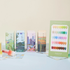The alt text for the image could be:
"A colorful display showcasing MAYOUR The Collector Season 2 gel polish set, featuring 40 semi-sheer lacquers in a variety of seasonal hues. The product packaging and display highlight the versatility, quality, and artistry of this premium nail care brand.