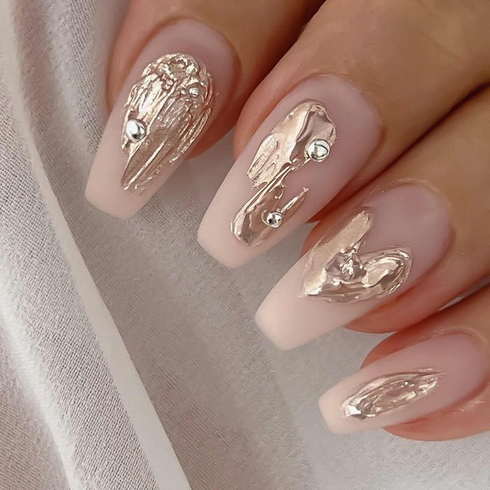 Elegant long almond-shaped nails with a nude base and intricate gold foil designs, showcasing the luxurious and artistic possibilities of Nailbayo DOI Thick Gel. The metallic accents create a fluid, abstract pattern, demonstrating the gel's versatility for high-end nail art and its ability to achieve a sophisticated, Korean-inspired manicure look.