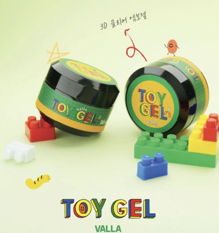 The image shows a Shopify product called "VALLA Toy Gel", which is a 3D clear clay gel that can be used for various creative purposes, such as 3D nail art. The product appears to be displayed with Lego-style blocks and other playful elements, highlighting its versatility and suitability for creative projects. The alt text for this image could be:

"VALLA Toy Gel - a 3D clear clay gel that can be rolled, squished, and sculpted for creative project