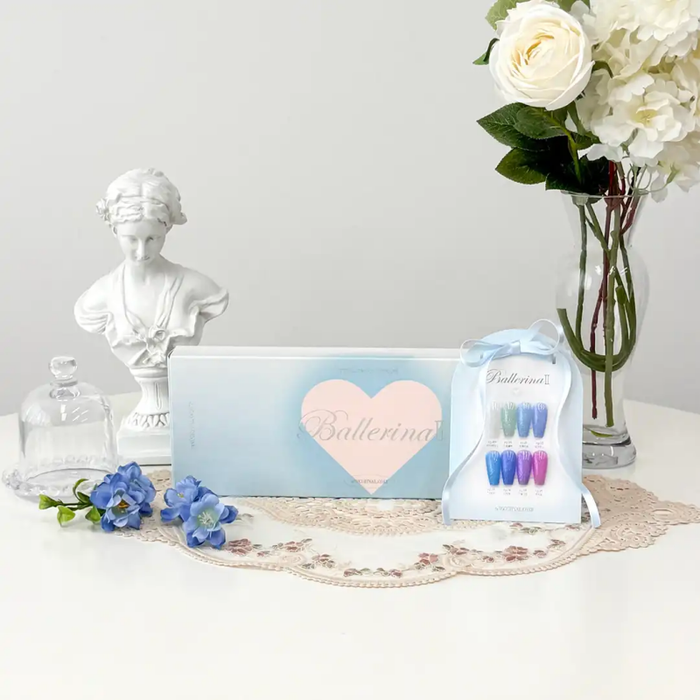 Elegant pastel-colored Ballerina 2 Collection box showcasing a heart-shaped logo, with a collection of colorful nail polish bottles, a vase of white flowers, and a decorative statuette, creating a serene and feminine ambiance, highlighting the premium, luxurious brand experience.